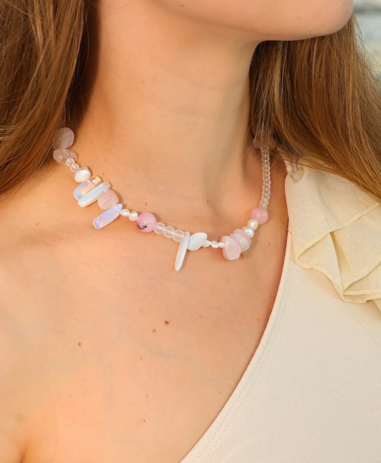 Soft pink tones and iridescent elongated accents create a luminous, asymmetric necklace.