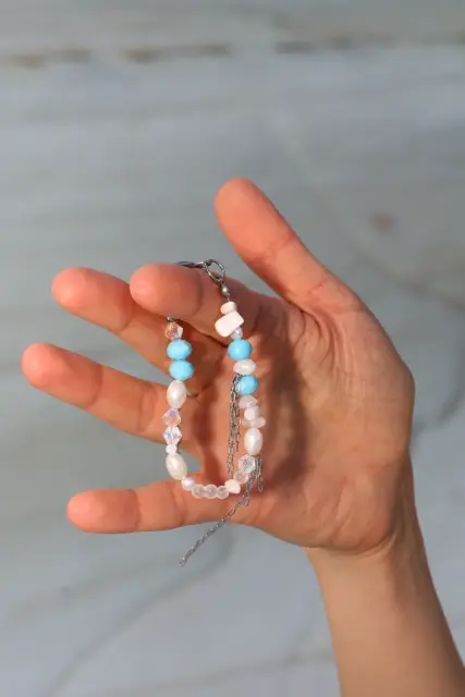 Bright blue accents, luminous white details and fine dangling chains create a playful bracelet full of movement.