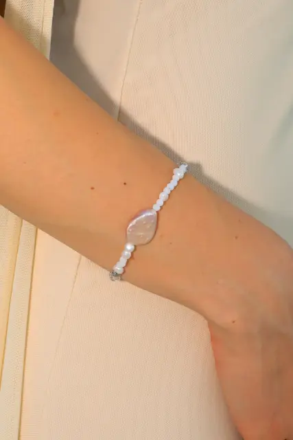 A luminous central pearl and delicate white details create a quiet, elegant accent for every day.